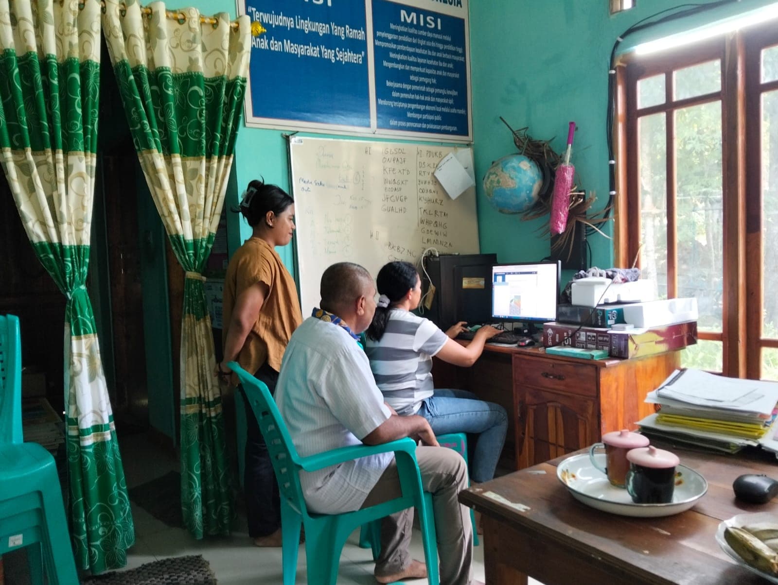 Pendampingan di depan komputer, di bawah papan visi dan misi yayasan